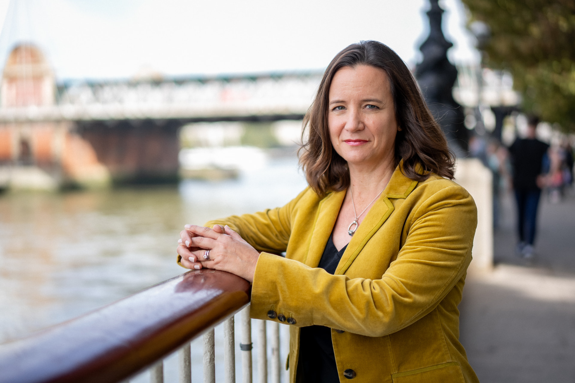 Kathryn Kernick standing by the river in a mustard jacket, smiling